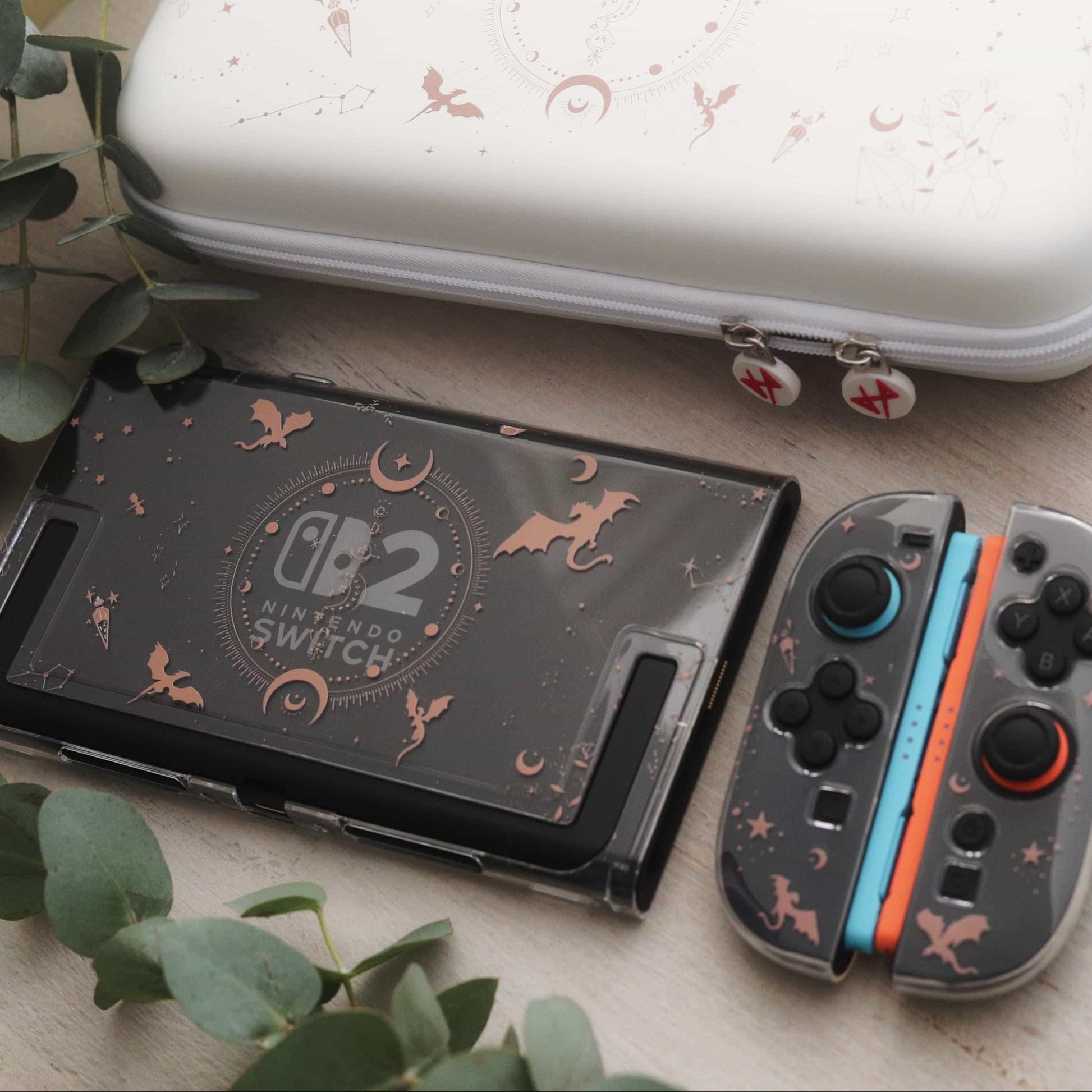 Emberwing Nintendo Switch 2 case with matching dragon and crescent moon print, paired with a white travel case on a eucalyptus-decorated surface.