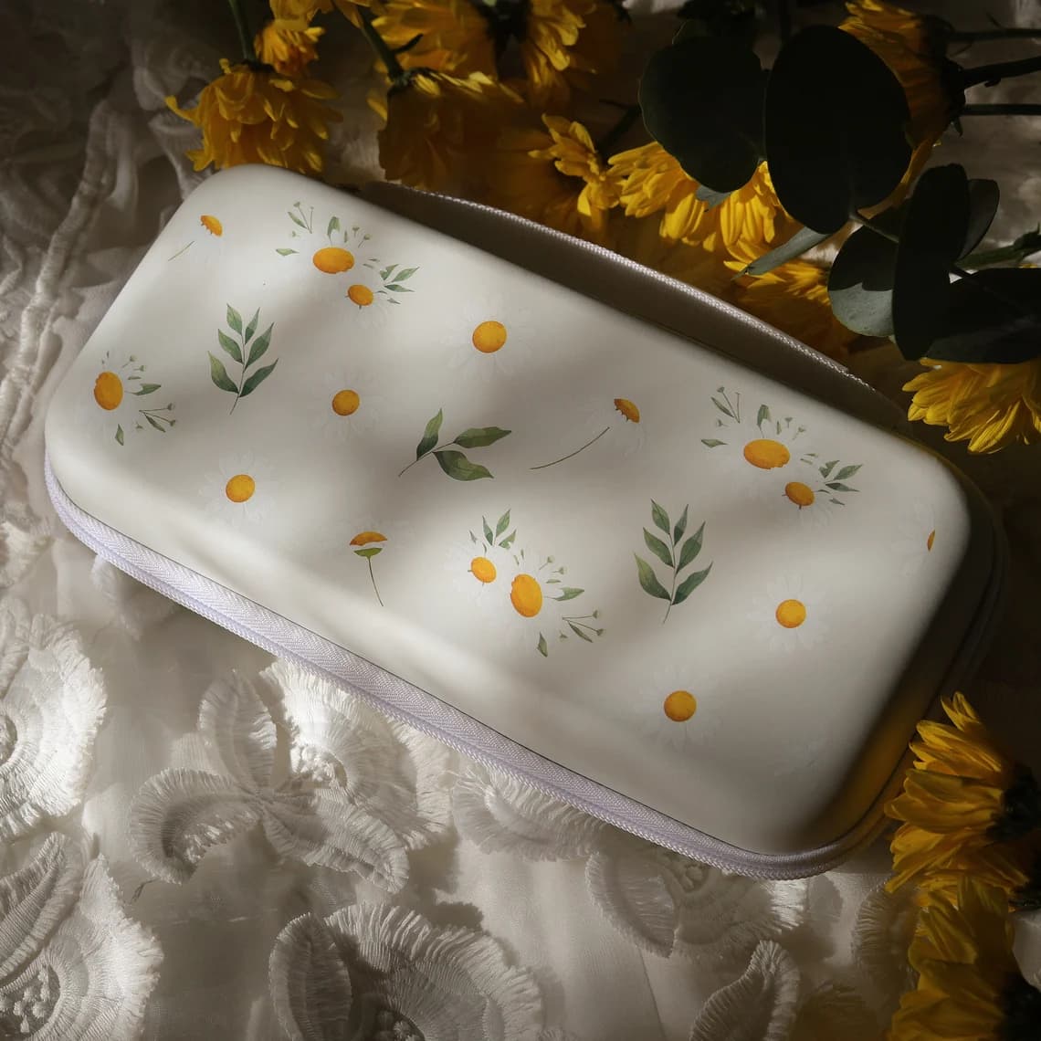 White Nintendo Switch Daisy Daydream carrying case with daisy and leaf pattern, styled with yellow flowers and eucalyptus