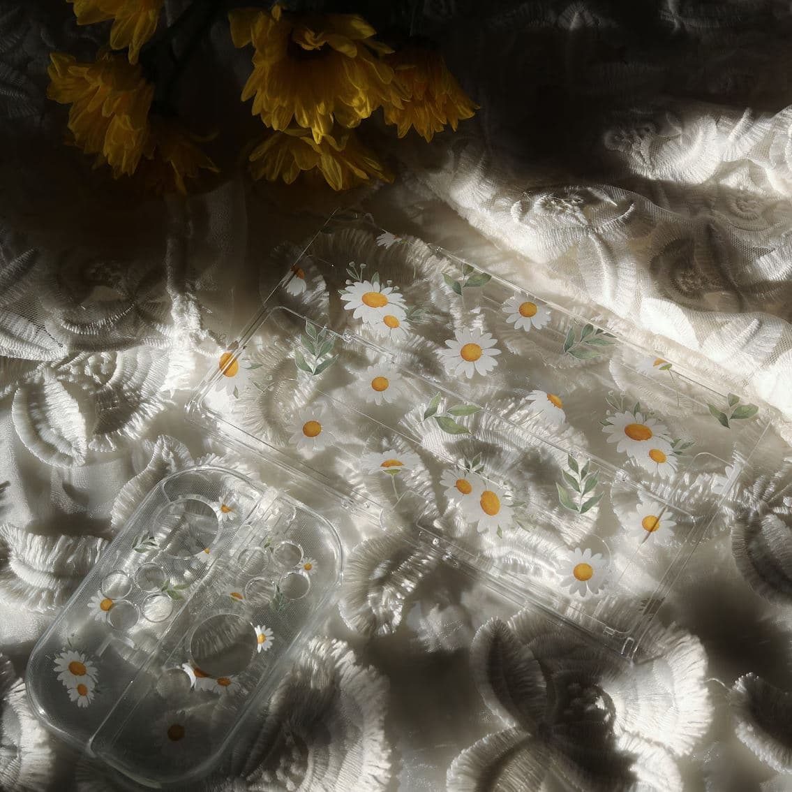 Flat lay of clear Nintendo Switch Daisy Daydream console shell and Joy-Con cases with daisy floral pattern on white fabric