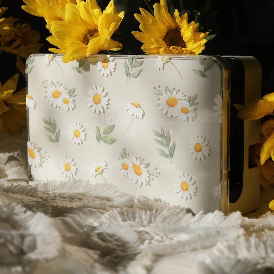 Clear Nintendo Switch dock cover with Daisy Daydream watercolour daisy and leaf pattern, styled upright with sunflowers